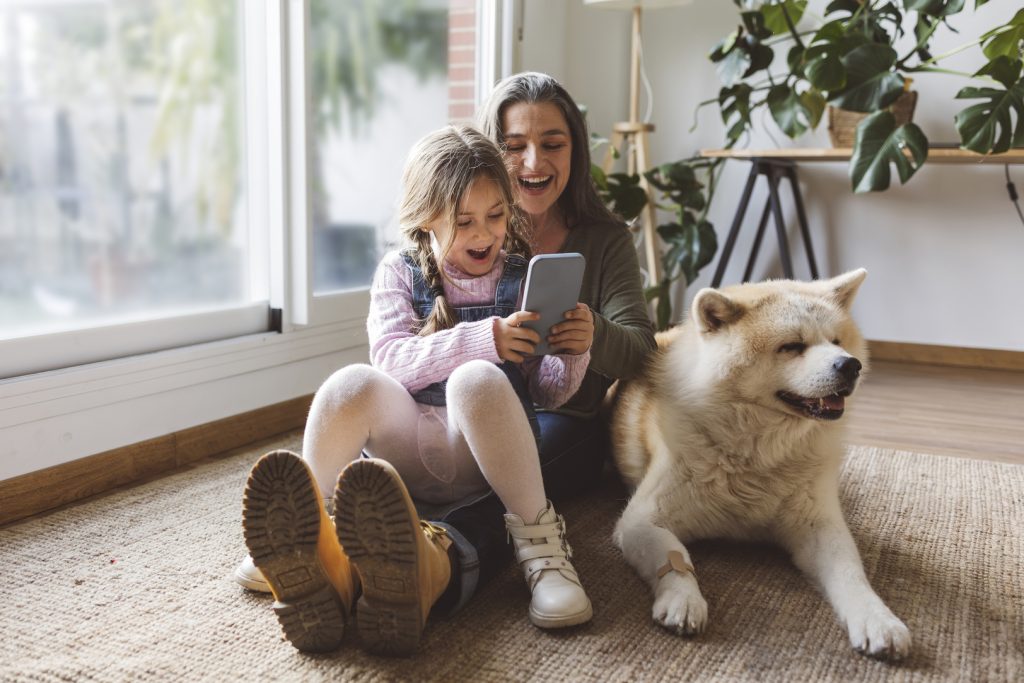 Mama en dochter zitten met hun hond op tapijt terwijl je ze een goedkoper mobiel abonnement afsluiten.