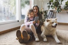 Mama en dochter zitten met hun hond op tapijt terwijl je ze een goedkoper mobiel abonnement afsluiten.