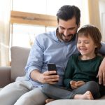Vader en zoon kijken naar de smartphone vanuit de zetel.