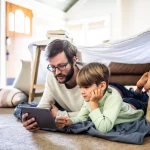 Vader en zoon liggen op tapijt en spelen een videospelletje