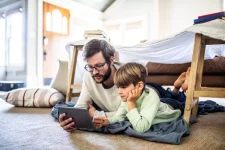 Vader en zoon liggen op tapijt en spelen een videospelletje