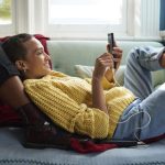 Vrouw ligt in zetel terwijl ze naar haar smartphone kijkt.