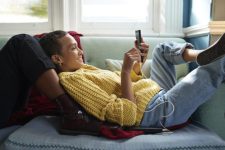 Vrouw ligt in zetel terwijl ze naar haar smartphone kijkt.