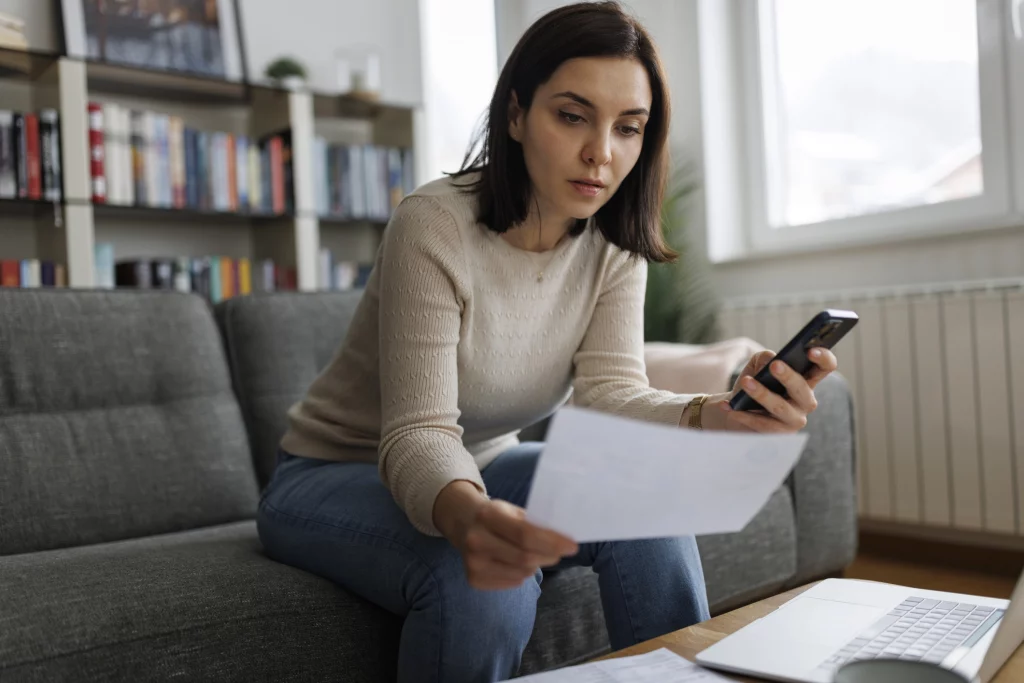 Vrouw met smartphone in de hand bekijkt factuur.