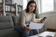 Vrouw met smartphone in de hand bekijkt factuur.