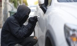 Dief probeert in te breken in witte auto die geparkeerd staat.