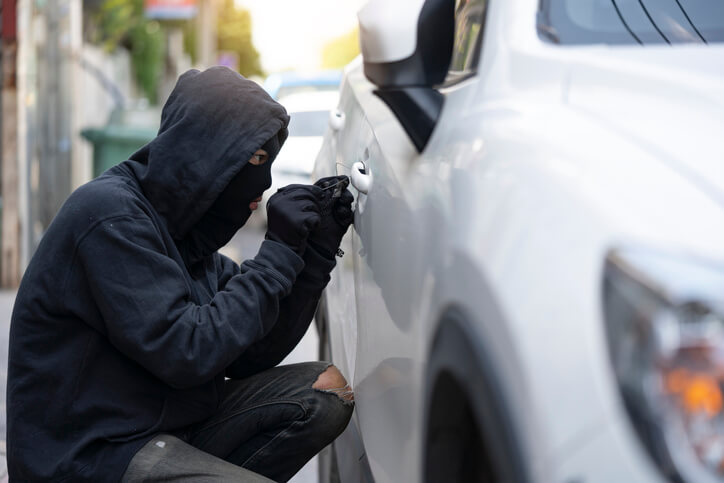 Dief probeert in te breken in witte auto die geparkeerd staat.
