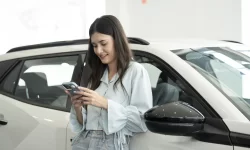 Vrouw staat tegen wagen en bekijkt haar smartphone.