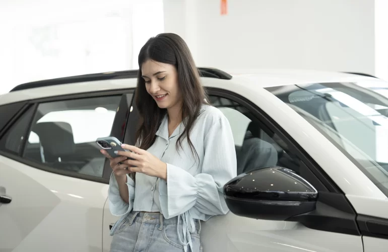 Vrouw staat tegen wagen en bekijkt haar smartphone.