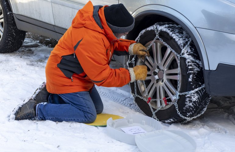 Man legt sneeuwkettingen op zijn autobanden.