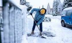 Actieve senior man maakt het voetpad sneeuwvrij met een sneeuwschop.
