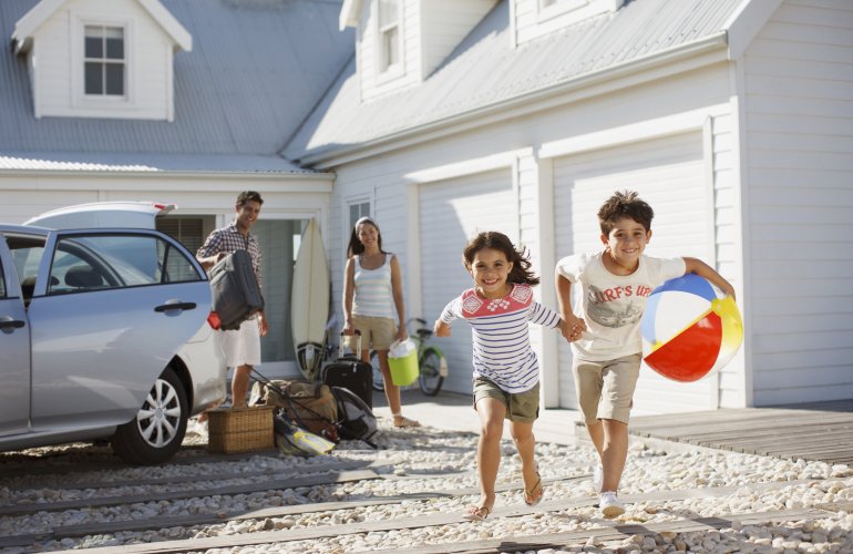 Familie-komt-toe-bij-hun-vakantiehuisje-en-kinderen-lopen-met-strandballen-rond