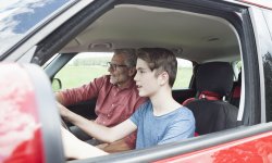 Jongen leert autorijden van zijn vader in een rode auto.