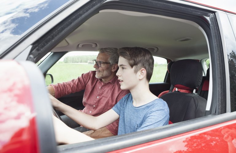 Jongen leert autorijden van zijn vader in een rode auto.